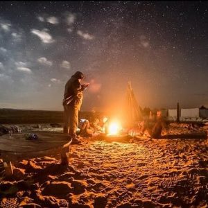 A desert camp set up for a Bedouin dinner, with people and traditional lighting in Hurghada