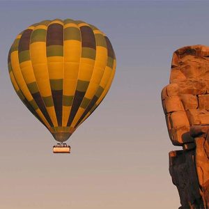 A hot air balloon floating above the ancient Colossi of Memnon in Luxor